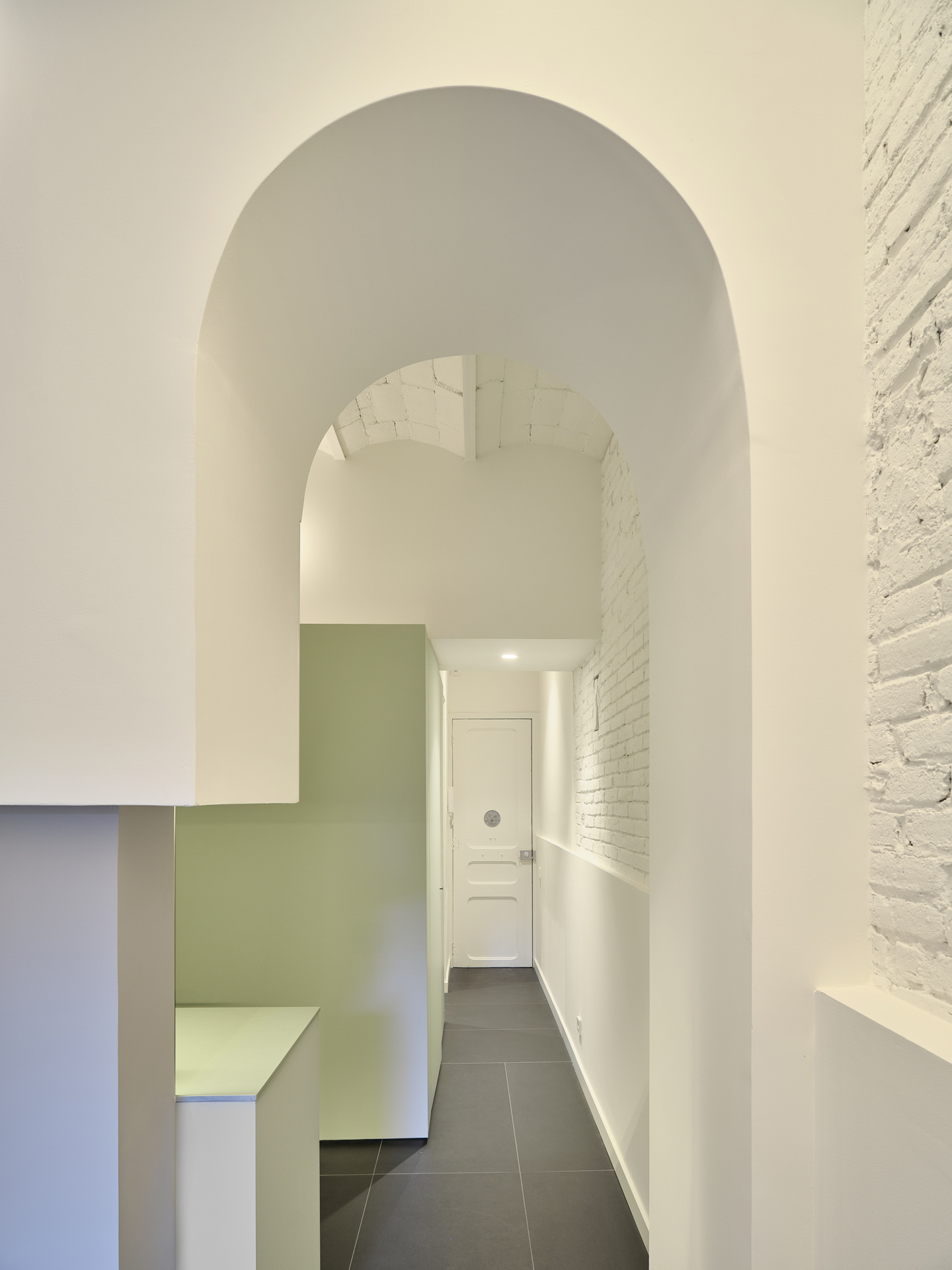 Arched corridor in CRÜ’s “La Dolors” renovation, featuring whitewashed brick walls, a soft green storage volume, and the original exposed ceramic ceiling.
